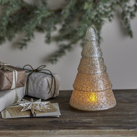 Emilius glass Christmas tree decoration in white, tiered fir shape with textured crackle finish, lit from within and displayed on a wooden surface with gifts and festive greenery.
