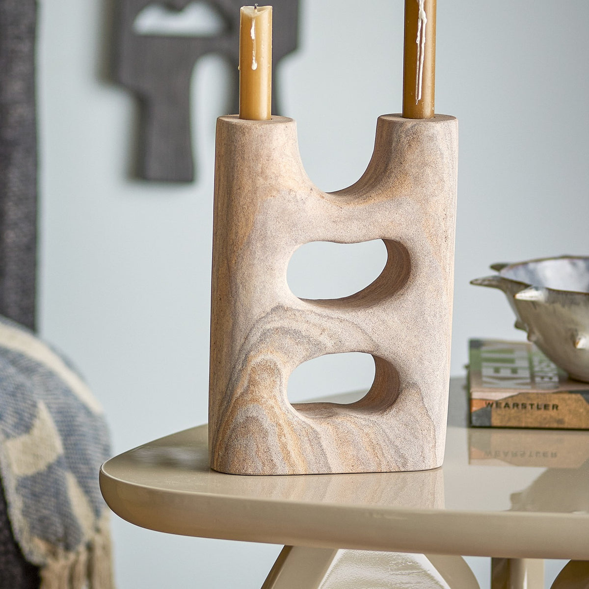 Lodi Marbled Sandstone Candle Holder in beige, a two-armed stone piece with pebble-like cut-through openings, holding two taper candles on a side table.