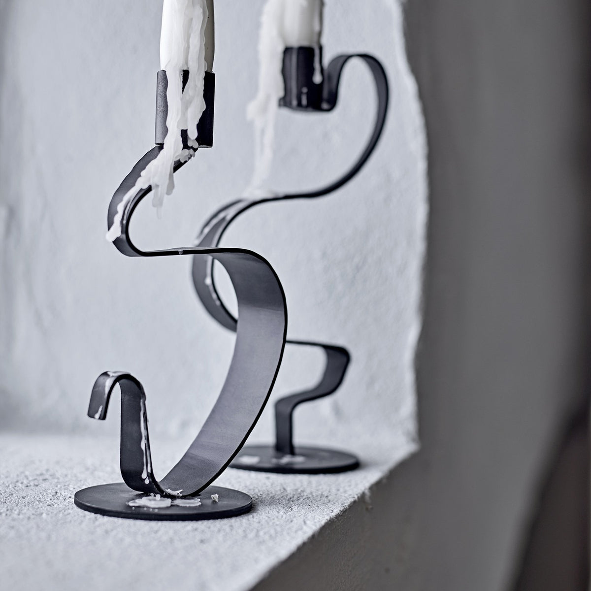 Do Iron Candle Holders Set of 2 in black, flat metal ribbon twisting up from a round base to a candle cup, shown with dripping candles on a light stone ledge.