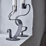 Do Iron Candle Holders Set of 2 in black, flat metal ribbon twisting up from a round base to a candle cup, shown with dripping candles on a light stone ledge.