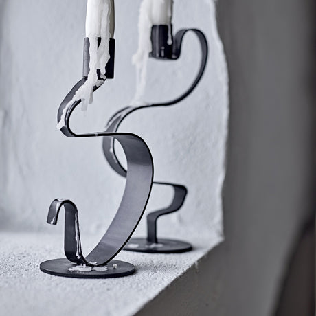 Do Iron Candle Holders Set of 2 in black, flat metal ribbon twisting up from a round base to a candle cup, shown with dripping candles on a light stone ledge.