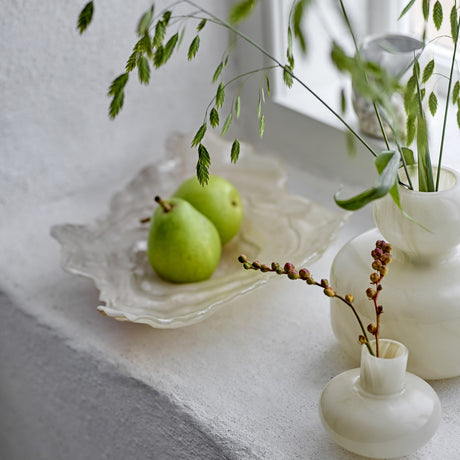 Aiku Shell Glass Bowl 38x29cm in pearl glass with rippled rim, holding green pears on a windowsill beside white bud vases and foliage.