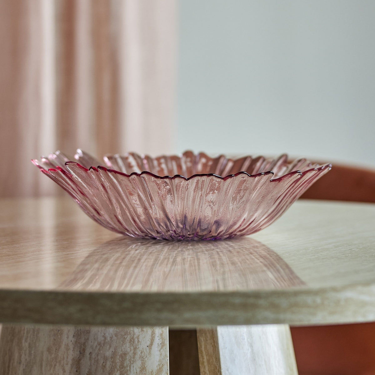 Mariko Flower Glass Bowl 31cm in pink, with a ruffled petal-edged rim and ribbed texture, shown on a wooden table in a dining room setting.