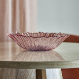 Mariko Flower Glass Bowl 31cm in pink, with a ruffled petal-edged rim and ribbed texture, shown on a wooden table in a dining room setting.