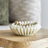 Harmonia Fluted Marble Bowl 17.5cm in white with deep pleated flutes and a wavy rim, holding dried seed pods on a wooden table.