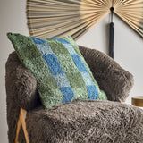 Pil Cotton Cushion in green, a square tufted cotton cushion with a checked pattern in blue and green, shown resting on a fluffy brown armchair.