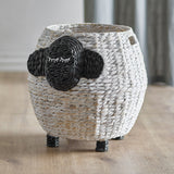 Dolly Sheep water hyacinth storage basket in white, with a dark woven face, ears and stitched closed eyes, raised on short woven legs on a wooden floor.