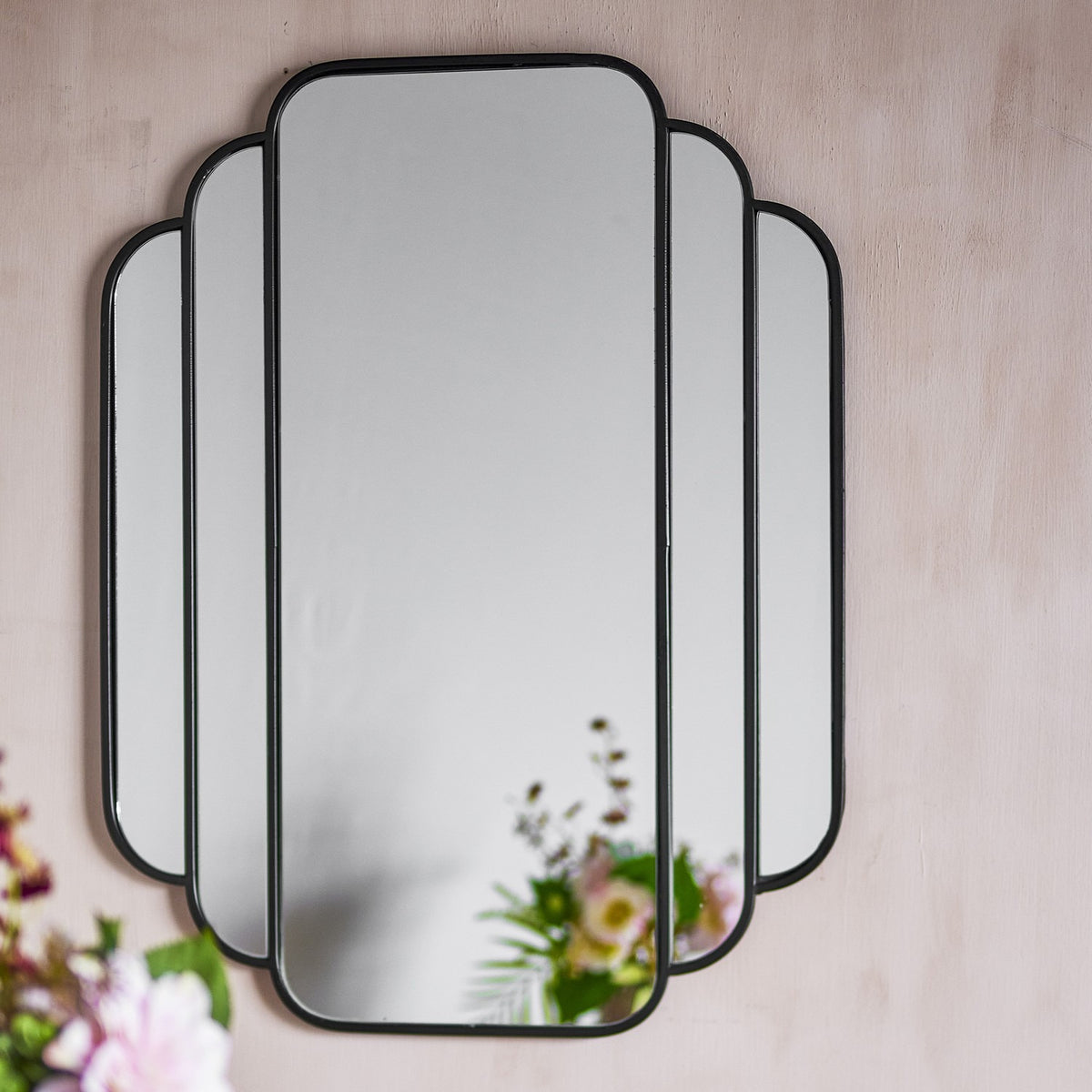Mas Iron Wall Mirror 63x80cm in black, featuring five stepped mirrored panels with slim rounded iron frames in a fan-like arrangement, mounted on a light wall near flowers.
