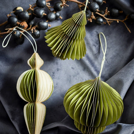 Tinkle Paper Christmas Tree Decorations, Set of 3 in green honeycomb paper, shown as a tiered tree shape and a layered bauble with hanging loops against dark fabric with berries.