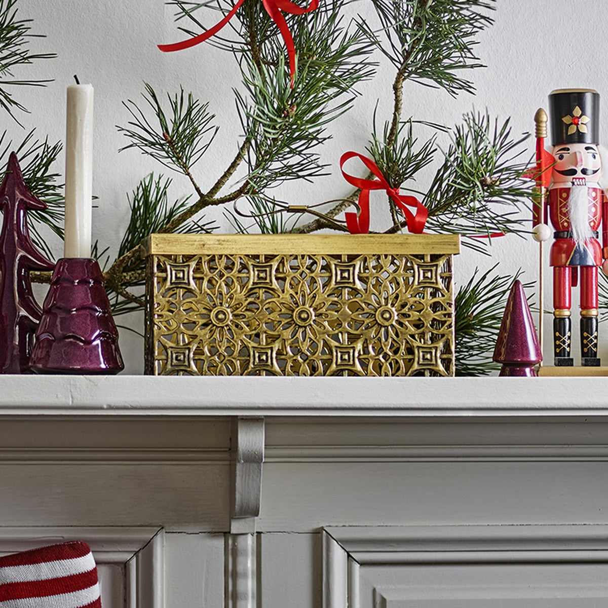 Gretl Floral Iron Christmas Storage Box with Lid in gold, shown on a mantel with a nutcracker, candle, and pine branches for festive styling.