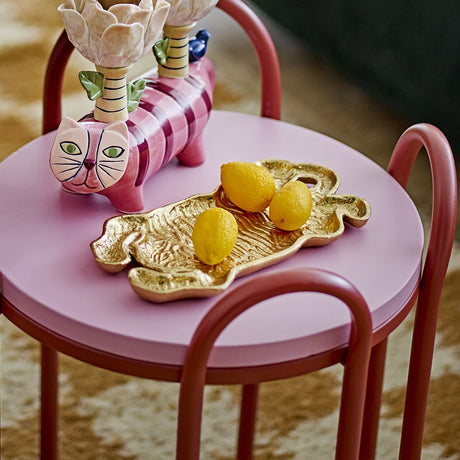 Lester Tiger Cast Iron Tray in gold, tiger-shaped with textured stripes and raised edge, holding lemons on a pink side table with a red metal chair.