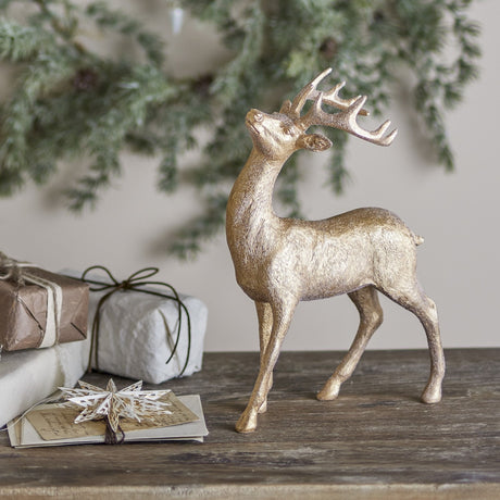 Pranzer Resin Christmas Decoration 30cm in Gold, a standing deer figurine with branching antlers and textured coat, displayed on a wooden surface beside gift boxes and greenery.