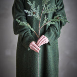 Pine Artificial Christmas Stem 91cm in Green, a faux branch with fine needles and small cones, held upright by hands over a green knit dress against a grey background.