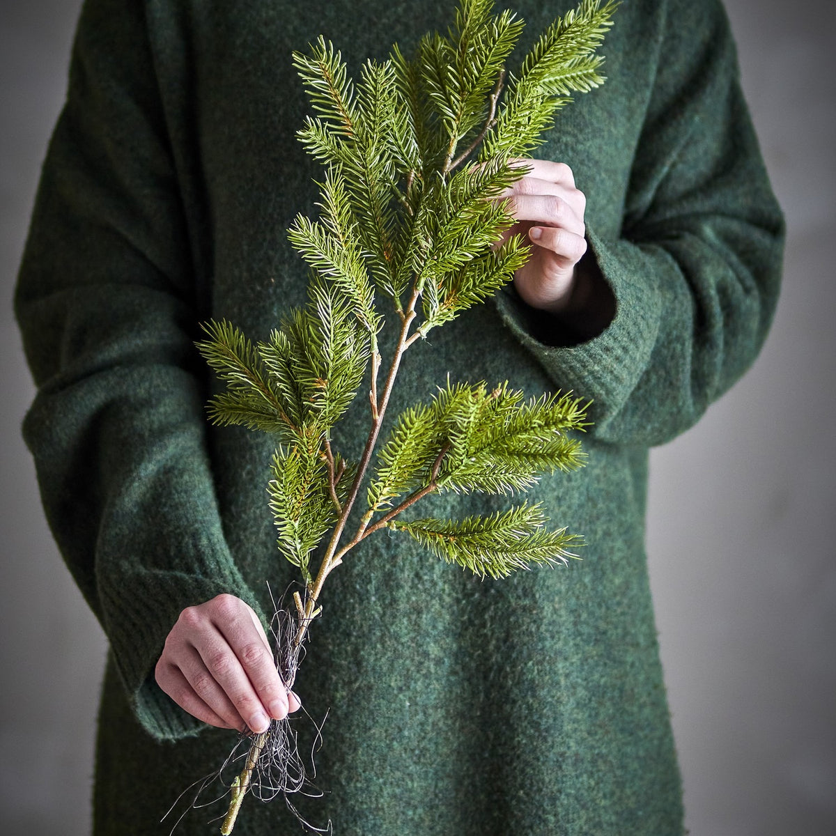 Pine Artificial Christmas Stem, 56cm, green faux pine branch with fine needles held in hand against a dark green sweater.