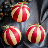 Wynn Striped Christmas Baubles, set of 3 red and cream thread-wrapped balls with beaded gold caps and hanging loops, shown on grey fabric with dark berries.