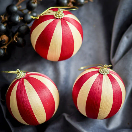 Wynn Striped Christmas Baubles, set of 3 red and cream thread-wrapped balls with beaded gold caps and hanging loops, shown on grey fabric with dark berries.