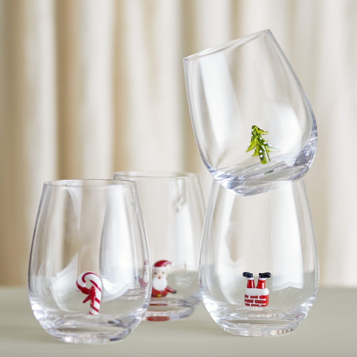 Misa Christmas Tumblers Set of 4 in clear glass, each stemless tumbler featuring a small figure inside—candy cane, waving Santa, Santa's boots in a chimney, or a Christmas tree.
