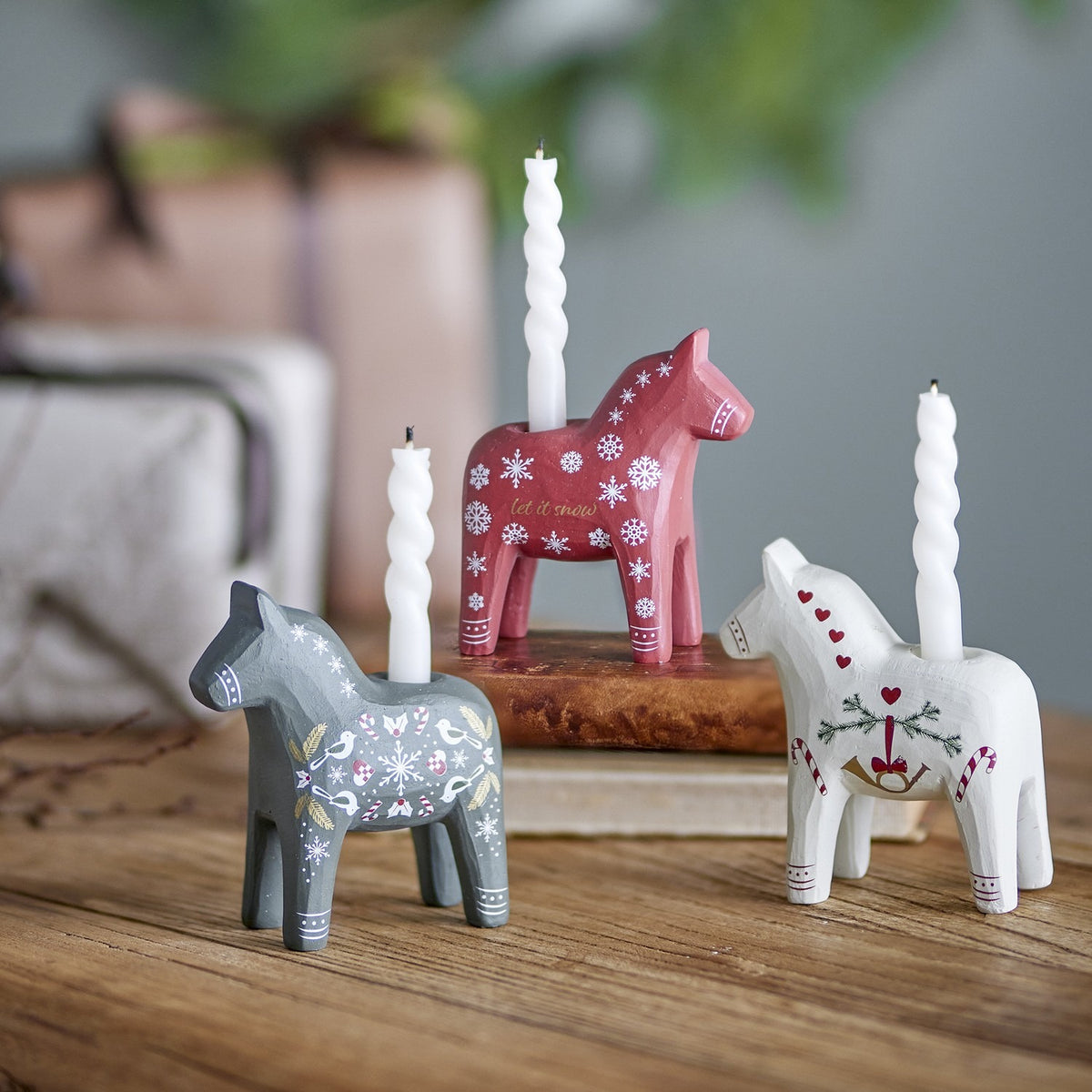Set of 3 resin folk-style horse candle holders in red, grey and white with hand-painted snowflakes, hearts and birds, each holding a white spiral candle.