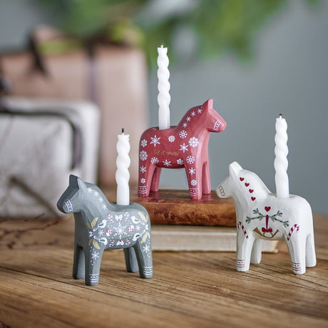 Set of 3 resin folk-style horse candle holders in red, grey and white with hand-painted snowflakes, hearts and birds, each holding a white spiral candle.