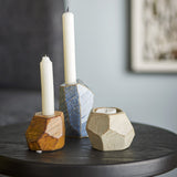 Kimber Stoneware Tealight & Candle Holders, set of three faceted stone-like pieces in rust, blue, and sandy tones, shown with white taper candles on a dark side table.