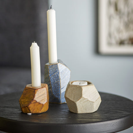 Kimber Stoneware Tealight & Candle Holders, set of three faceted stone-like pieces in rust, blue, and sandy tones, shown with white taper candles on a dark side table.