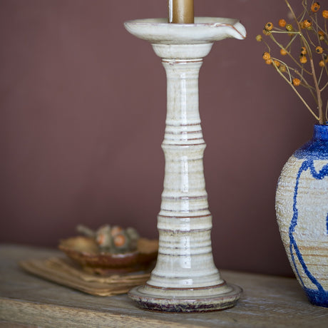 Rigby Stoneware Candle Holder in grey, a turned column with ringed stem and flared foot, shown on a wooden surface beside a dried floral arrangement.