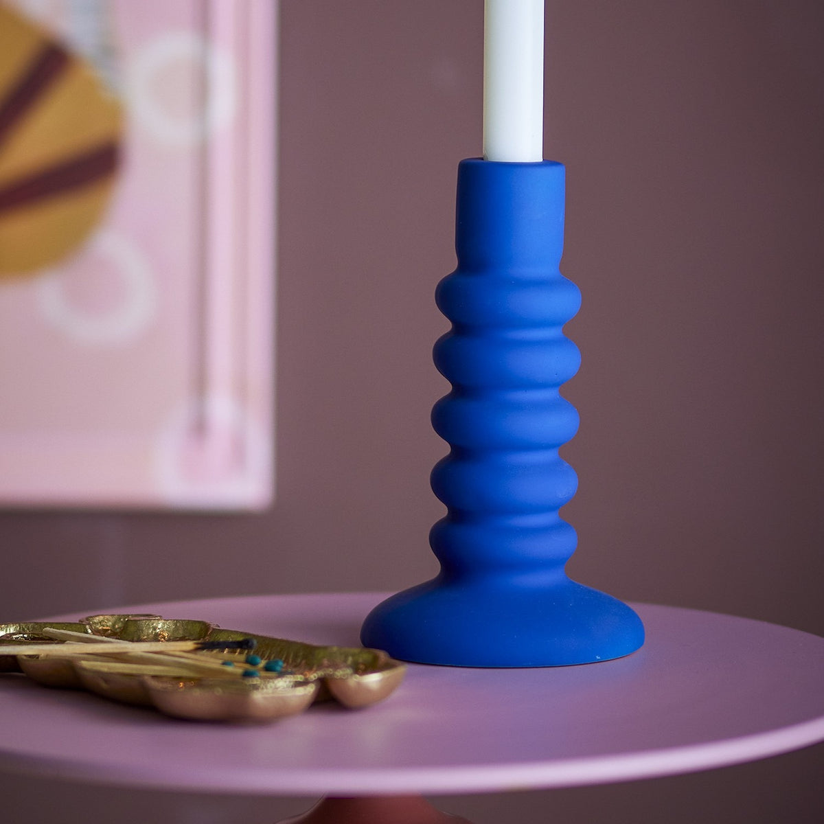 Thorne Stoneware Candle Holder in matte blue, 18.5cm tall with ridged rings and a flared foot, holding a white taper candle on a pink table.