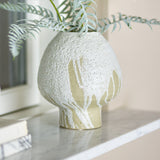 Morag Mushroom Stoneware Vase 19cm in White, with a rounded mushroom-shaped body in pitted, speckled glaze breaking into streaks near the foot, shown on a marble shelf with trailing foliage.
