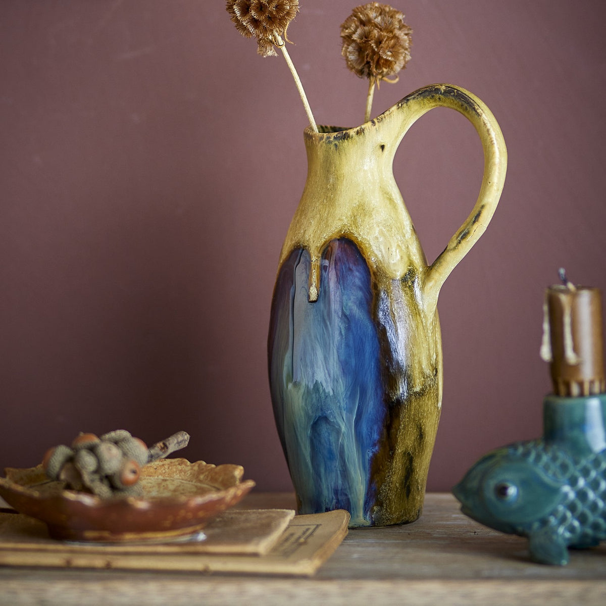Jenkins Stoneware Vase 20cm in Multi, a slender jug-shaped ceramic vase with a tall looped handle and multicoloured glaze dripping from neck to base, shown with dried flowers on a tabletop.