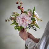 Splendor Artificial Bouquet in Pink held by hand, showing a large pink dahlia with ferns, berries and sprigs against a plain light background.