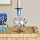 Phila Glass Candle Holder in Blue, a clear glass puffer fish-shaped candle holder with blue glass spines and a flared blue cup, holding a candle on a woven side table.