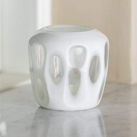 Rohan Glass Tealight Holder in white, a rounded glass candle holder with recessed teardrop cutouts, shown on a marble surface.