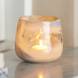 Imran Marbled Glass Tealight Holder in grey, a rounded recycled-glass votive with swirled marbling, shown lit on a marble surface.