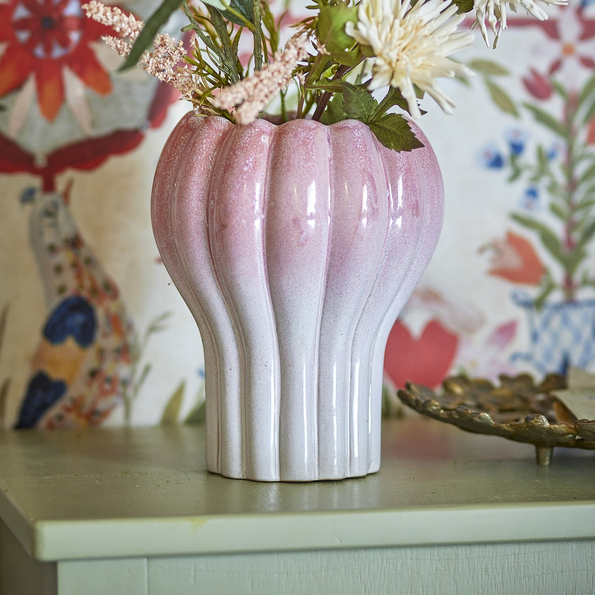 Kyla Stoneware Plant Pot in pink, fluted ceramic design with scalloped rim, shown holding dried florals on a pale sideboard against patterned wallpaper.