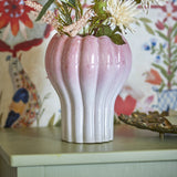 Kyla Stoneware Plant Pot in pink, fluted ceramic design with scalloped rim, shown holding dried florals on a pale sideboard against patterned wallpaper.