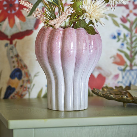 Kyla Stoneware Plant Pot in pink, fluted ceramic design with scalloped rim, shown holding dried florals on a pale sideboard against patterned wallpaper.