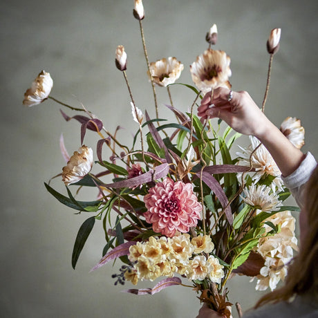 Hazy Artificial Bouquet in cream, shown being arranged by hand, with poppy-like blooms, buds on slender stems, a pink dahlia-style flower, and trailing foliage.
