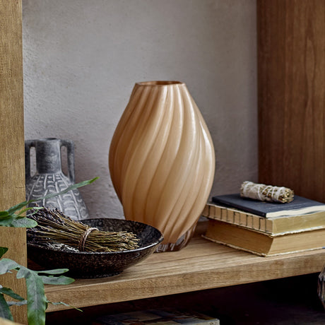Kanji Glass Vase 30cm in beige with spiral fluted ribs, shown on a wooden shelf beside books, a dark bowl, and a patterned ceramic jug.