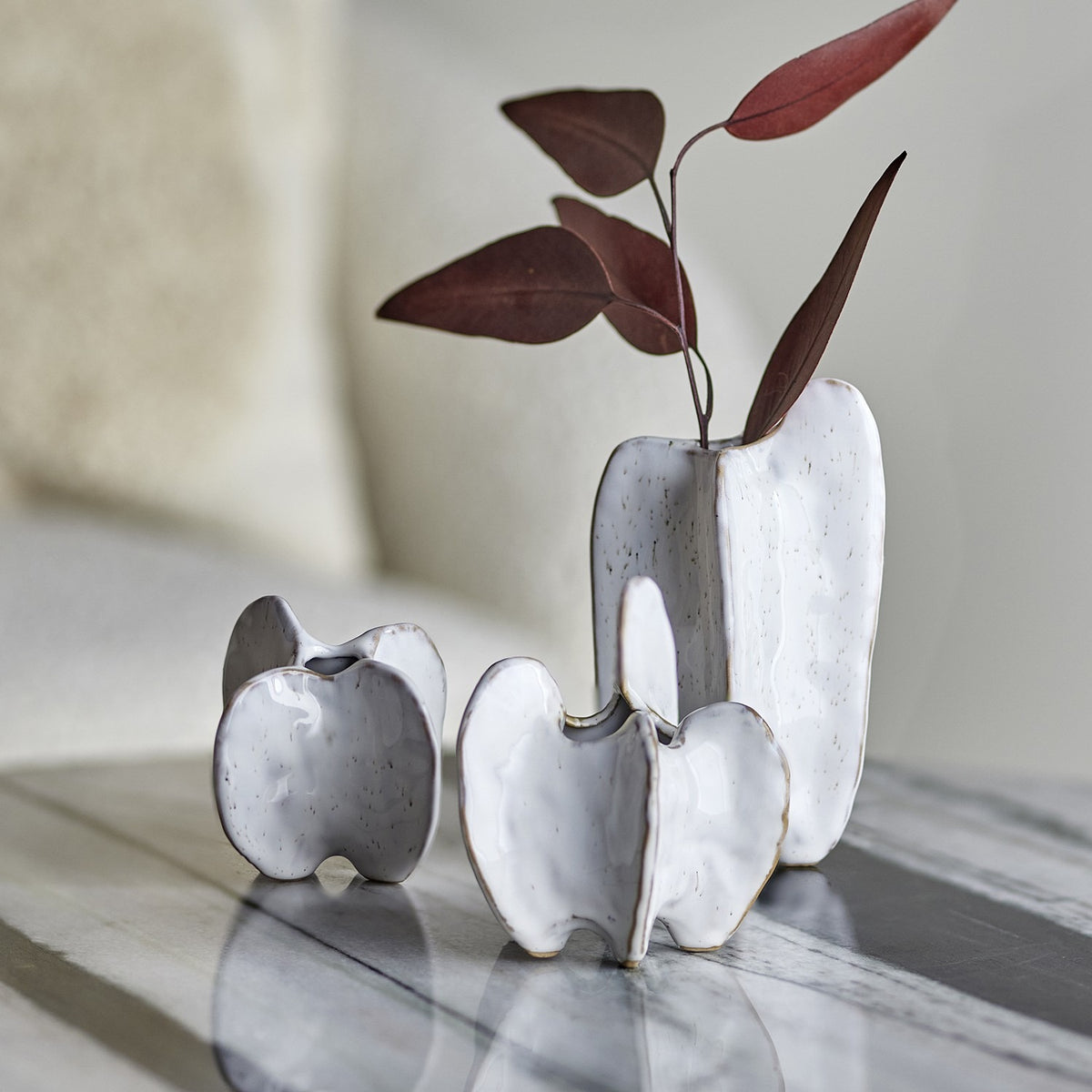 Jayce Stoneware Vases Set of 3 in white, sculptural lobed shapes with narrow openings in varying heights, displayed on a marble surface with a dried leaf stem in the tallest vase.