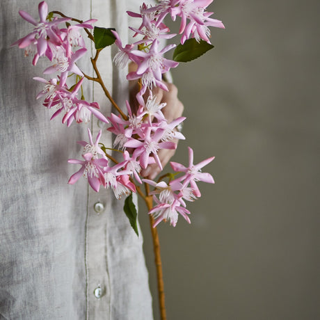 Artificial chrysanthemum stem, 72cm, with clusters of small pink star-shaped flowers and green leaves on a bare stem, held against a person's linen shirt.