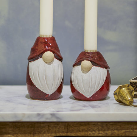 Lyda Stoneware Christmas Candle Holders Set of 2 in red, gnome-shaped with hats, round noses and sculpted beards, holding cream candles on a marble surface.