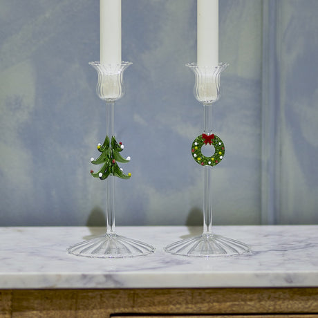Set of 2 Branton clear glass Christmas candle holders with fluted cups, ribbed flared feet, and wreath and tree stem details, shown with white candles on marble.