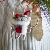 Grey felt mouse pair Christmas tree decoration hugging a red heart, with holly sprig, pompom Santa hat and white scarf, shown hanging near a sweater and pine branch.