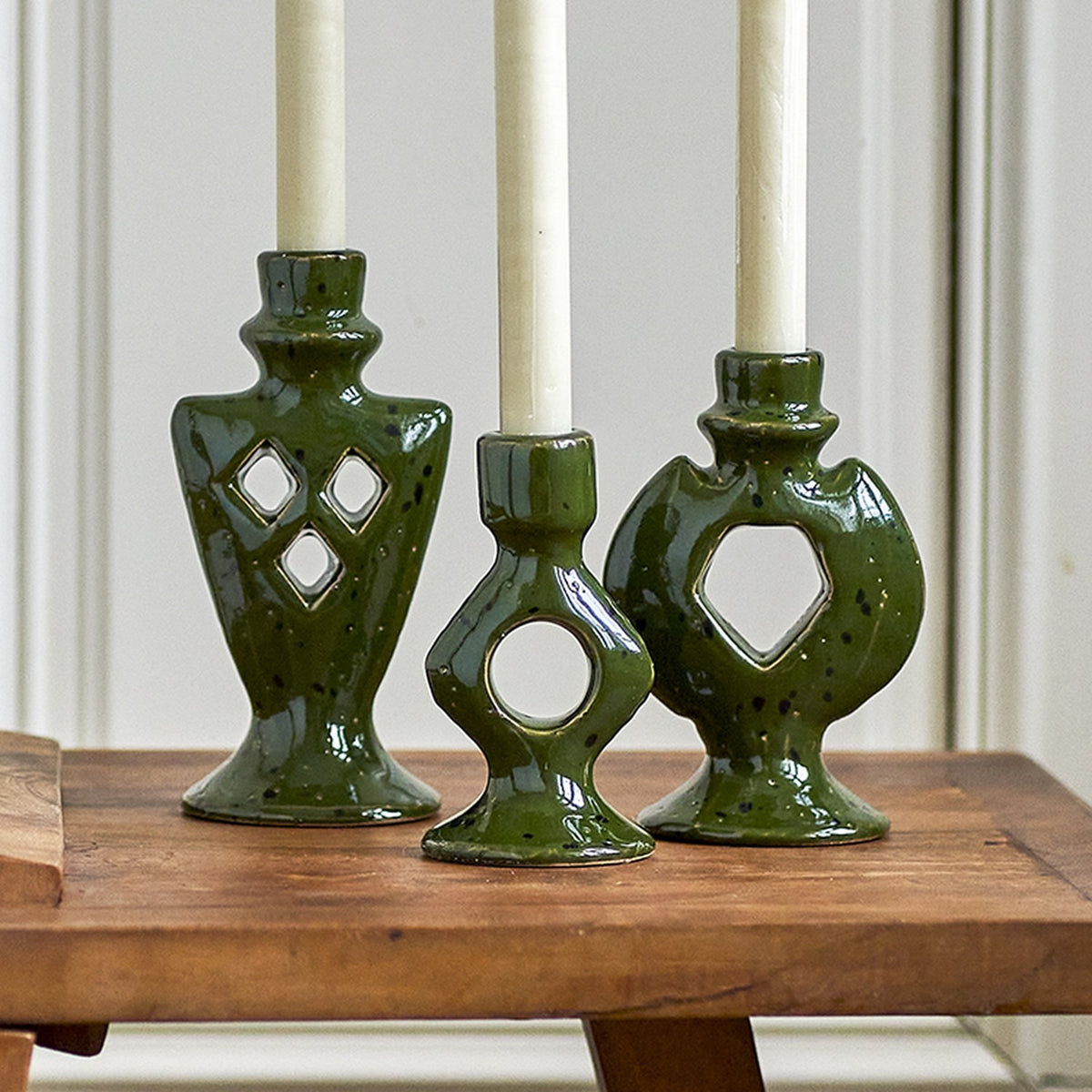 Weio green stoneware candle holders, set of 3 with geometric cut-outs, holding white taper candles on a wooden table.