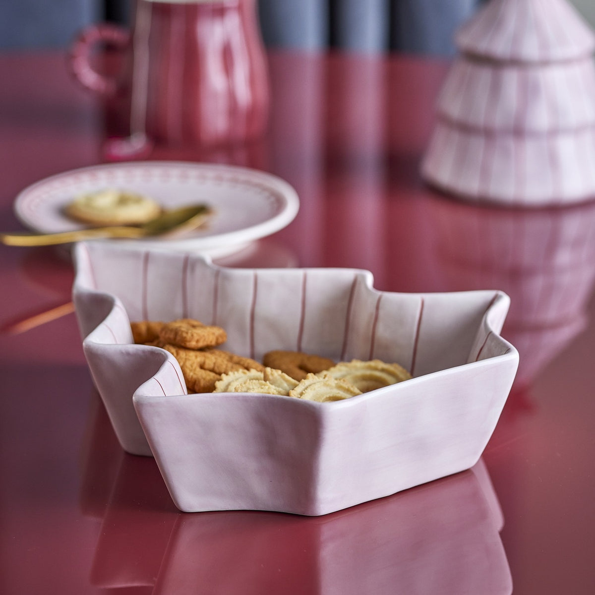 Shirly Striped Stoneware Christmas Platter in pink, a star-shaped serving dish with hand-painted pink stripes, shown filled with biscuits on a pink table setting.