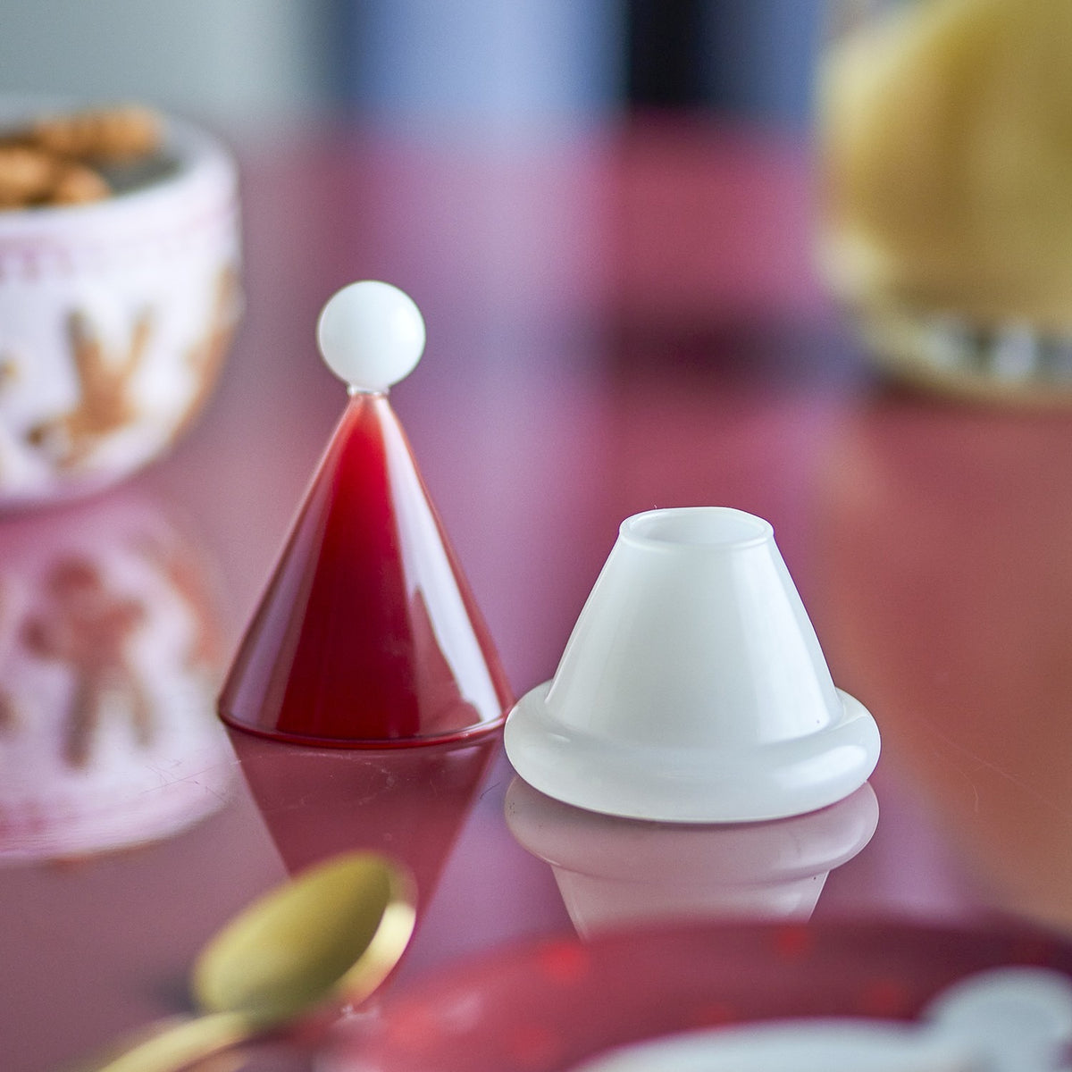 Patrice Glass Christmas Toothpick Holder in red, shaped like a Santa hat with a white ball-tip cone lid and white cup base, shown on a reflective red table.