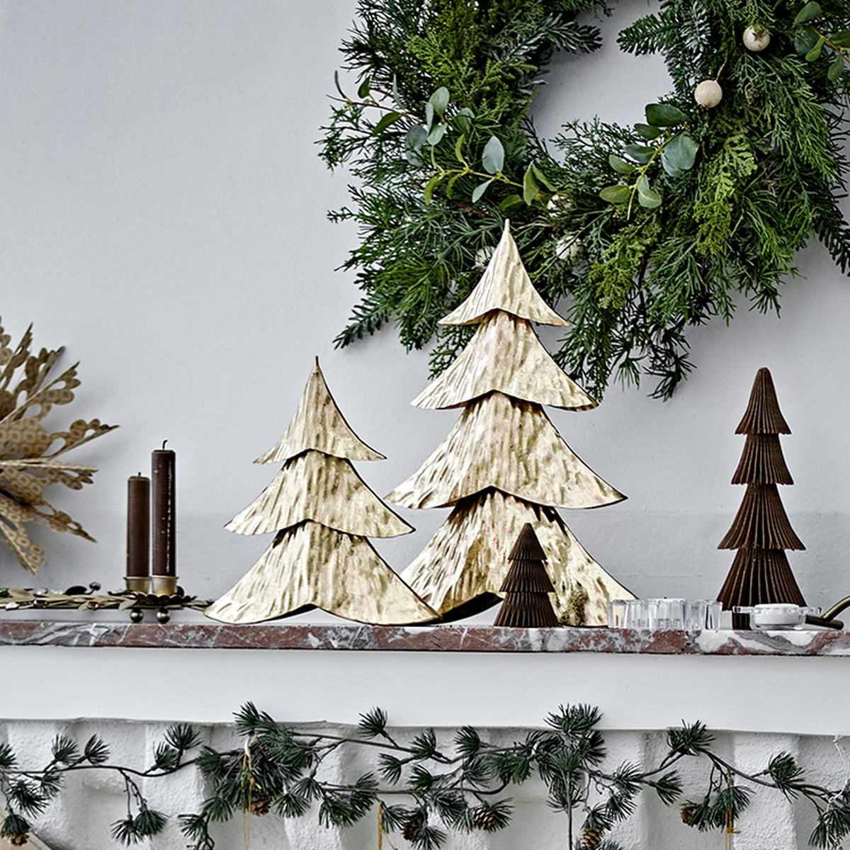 Kaiam Iron Christmas Decorations Set of 2 in gold, two tiered fir-tree ornaments with dimpled texture, displayed on a mantel with candles and a wreath.