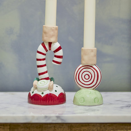 Set of 2 Leiani ceramic Christmas candle holders, a red-and-white candy cane and a striped round sweet, each with ivory candles, displayed on marble.