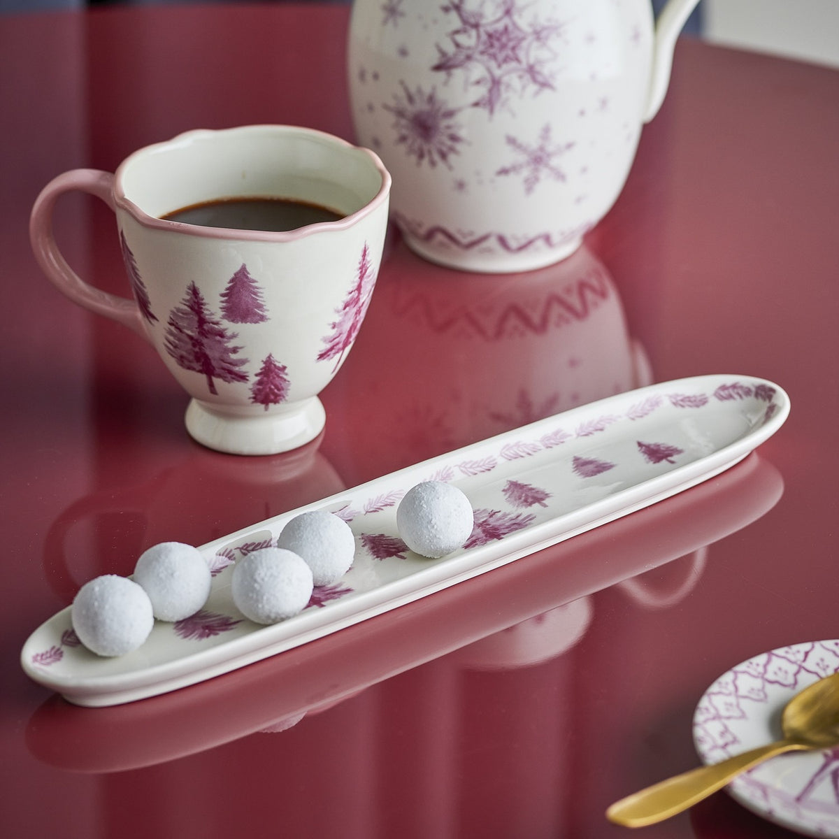 Wonderland Stoneware Christmas Platter in cream, long narrow shape with pine tree design and branch-patterned rim, shown with sugared truffles beside a matching mug and teapot.