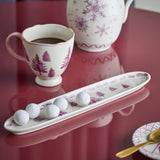 Wonderland Stoneware Christmas Platter in cream, long narrow shape with pine tree design and branch-patterned rim, shown with sugared truffles beside a matching mug and teapot.